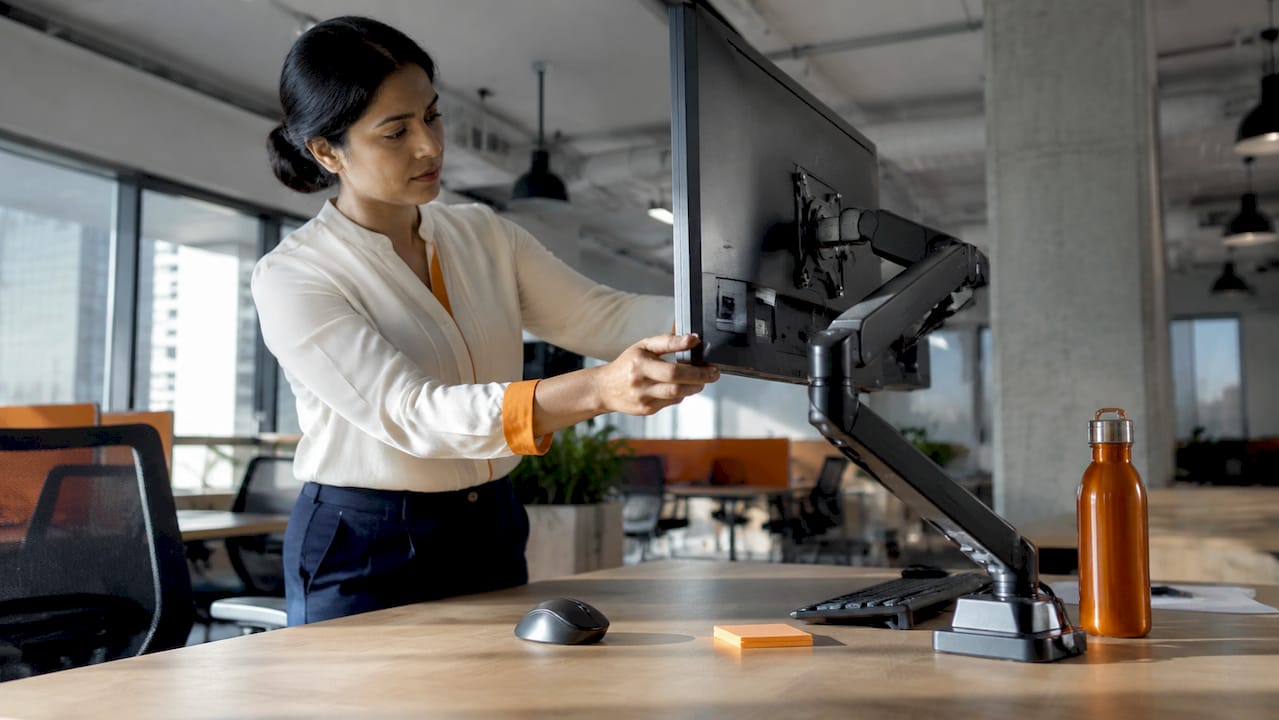 Woman adjusting ergonomic monitor arm at office desk